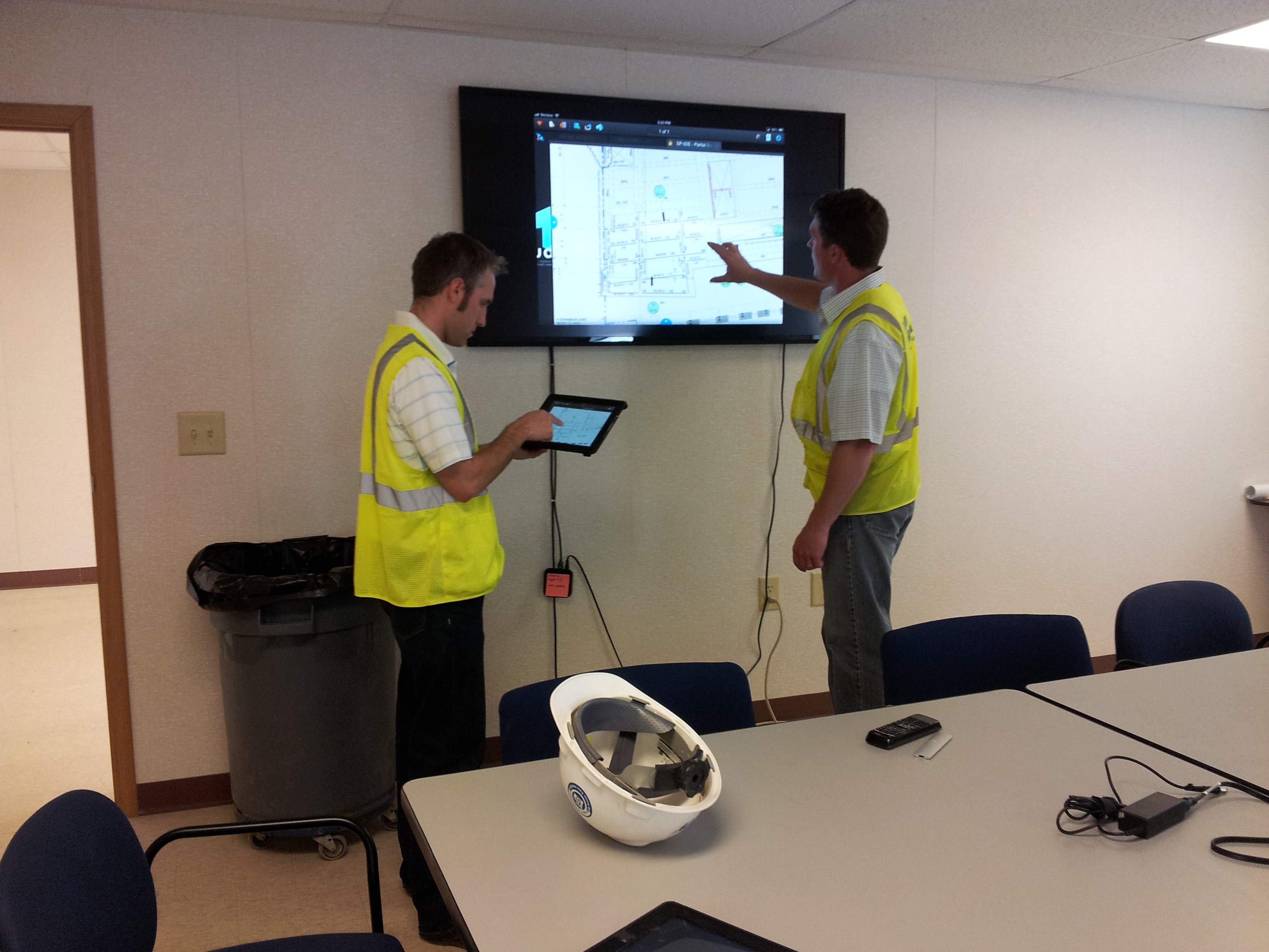 Two standing construction workers plan out their next move on a digital screen.